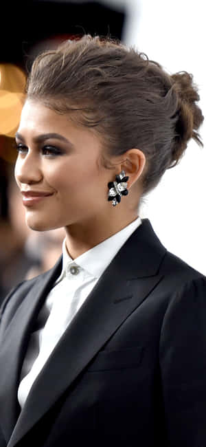 Zendaya 身穿黑色西裝和白色襯衫，戴著花卉耳環，在活動中微笑。 — 善逸大頭貼 壁紙