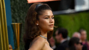 Zendaya 在正式活動中穿著迷人的晚裝，身後有綠植。 — 桌面 壁紙