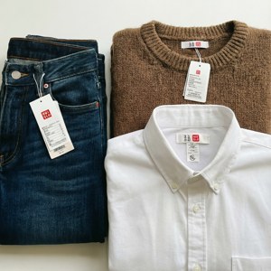 三件折疊的Uniqlo衣物，包括牛仔褲、毛衣和襯衫，標籤可見。 — Galaxy Watch 壁紙