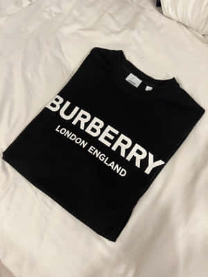 黑色Burberry T恤，白色文字，折疊在白色床上。 — Burberry 壁紙