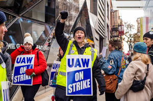 一群人在城市街道上抗議，手持UAW ON STRIKE標語牌，戴著冬帽和夾克。 — 人物 壁紙