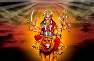 多臂印度教女神騎著獅子，背景是熾熱的日落天空。 — Maa Durga 壁紙
