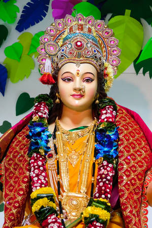 一尊裝飾華麗的神像，佩戴金色珠寶和色彩繽紛的花環。 — Maa Durga 壁紙