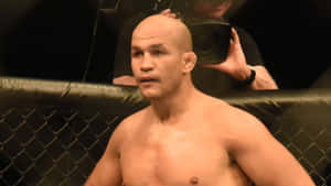 一位光頭MMA戰士在黑色八角籠內，身後有一名攝影師。 — 運動 壁紙