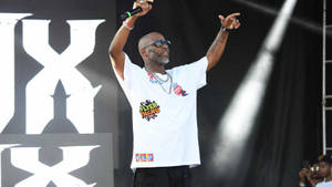 饒舌歌手在舞台上高舉雙臂，戴著太陽眼鏡和白色T恤表演。 — DMX 壁紙