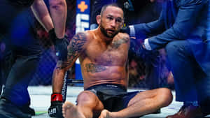 筋疲力竭的刺青MMA拳手坐在八角籠地上，醫護人員正在檢查他。 — 終極格鬥冠軍賽 壁紙