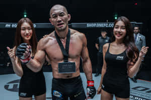 MMA拳手掛著冠軍獎牌，兩旁有兩位身穿黑色服裝的擂台女郎。 — 運動 壁紙