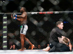 UFC拳手在八角籠中慶祝勝利，裁判照顧對手。 — 終極格鬥冠軍賽 壁紙