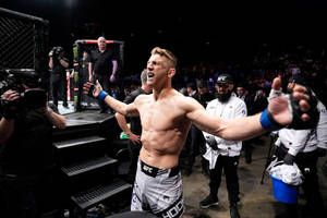 UFC拳手在八角籠中伸展雙臂慶祝勝利。 — 運動 壁紙