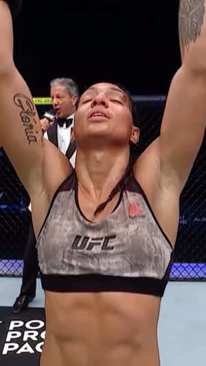 女性MMA拳手在八角籠內高舉雙臂慶祝勝利。 — 終極格鬥冠軍賽 壁紙