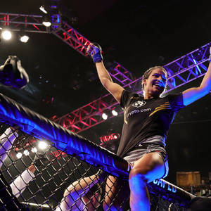 女性MMA拳手在八角籠中於明亮燈光下慶祝勝利。 — 運動 壁紙