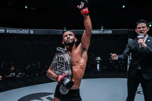 MMA拳手在八角籠中手持冠軍腰帶慶祝勝利。 — 運動 壁紙