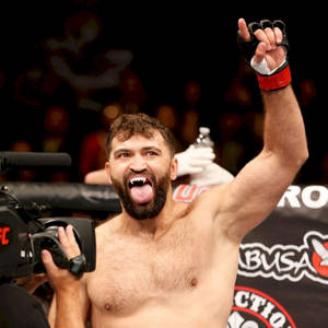 MMA拳手在八角籠中舉起拳頭並伸出舌頭慶祝勝利。 — 終極格鬥冠軍賽 壁紙