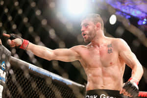 一位汗流浹背的MMA拳手在八角籠中以指向的姿勢慶祝勝利。 — 運動 壁紙