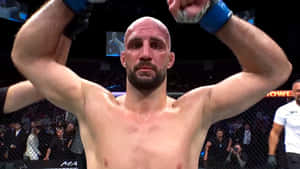 一位光頭鬍鬚的MMA拳手在八角籠內高舉拳頭慶祝勝利。 — 終極格鬥冠軍賽 壁紙
