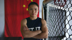 女MMA戰士雙臂交叉站在中國國旗和籠前。 — 運動 壁紙