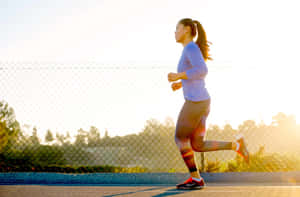 一位女士在日出時於小徑上慢跑，身後有鏈條圍欄。 — Running 壁紙