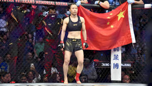 女性MMA拳手在UFC八角籠中手持中國國旗，觀眾觀看。 — 運動 壁紙