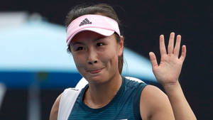 網球運動員微笑著向人群揮手，戴著粉紅色遮陽帽和藍色上衣。 — 運動 壁紙