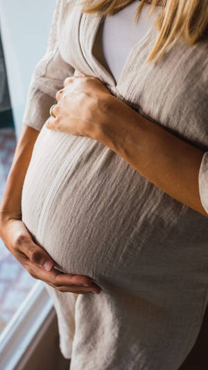 孕婦在窗邊柔和光線中捧著肚子。 — 懷孕 壁紙