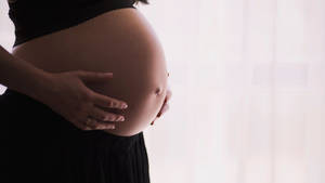 一位孕婦在窗邊用一隻手托著肚子。 — 懷孕 壁紙