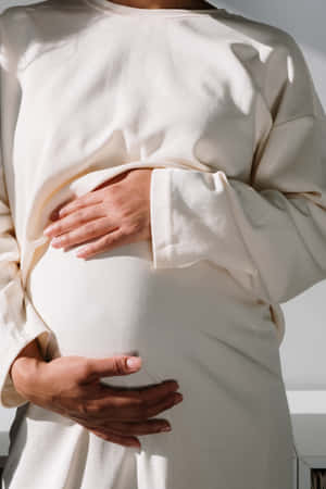 一位孕婦在柔和陽光中用雙手抱著肚子。 — 懷孕 壁紙