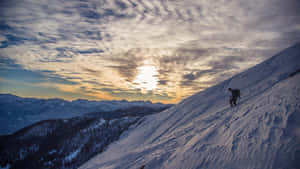 一位攀登者在日出時攀登積雪的山坡，遠方山峰清晰可見。 — iMac 壁紙