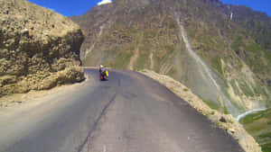 機車騎士在藍天下沿著蜿蜒山路行駛，兩旁是陡峭的懸崖和綠色的山坡。 — 印度 壁紙