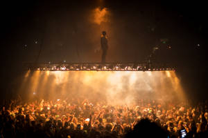 夜間音樂會中，高架舞台上的剪影表演者與歡呼的人群。 — 肯伊·威斯特 壁紙