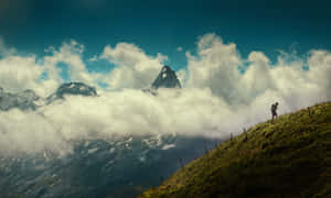 遠足者攀爬草坡，背景有雲霧和積雪的山峰 — 登山 壁紙