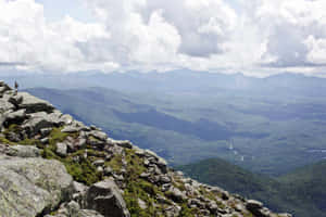 一個人站在岩石山峰上，俯瞰著森林覆蓋的山谷。 — 山坡 壁紙