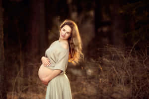 孕婦在陽光明媚的森林中輕柔地抱著腹部。 — 懷孕 壁紙