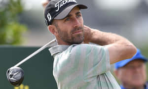 揮桿中的男性高爾夫球手，戴著 Titleist 帽子和條紋襯衫。 — 低調 壁紙