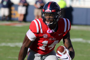 奧萊密斯美式足球員在草地場上於日落時帶球奔跑。 — Dk Metcalf 壁紙