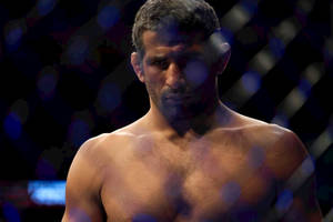 一位赤裸上身的MMA拳手在籠內帶著專注的表情。 — 運動 壁紙