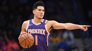 籃球運動員穿著鳳凰城太陽隊球衣，在比賽中持球並指向某處。 — Devin Booker 壁紙