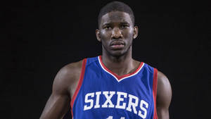 身穿Sixers球衣的職業籃球運動員專注地看著鏡頭。 — 喬爾·恩比德 壁紙