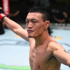 一位赤裸上身的MMA拳手在八角籠內舉起戴著紅色手套的拳頭慶祝勝利。 — 運動 壁紙
