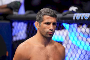 一位灰髮、赤裸上身的MMA選手在藍色燈光的八角籠中專注凝視。 — 運動 壁紙