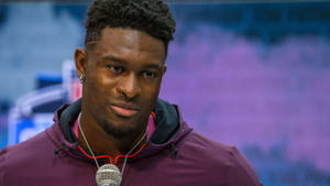 穿著紫色連帽衫的運動員在室內活動中對著麥克風說話。 — Dk Metcalf 壁紙