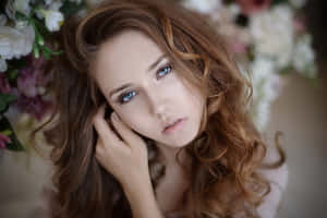 一位藍眼睛、捲髮的女子，被花朵環繞，輕輕地將下巴擱在手上。 — 模特兒 壁紙