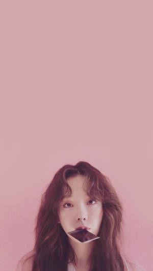 女性嘴裡含著巧克力棒，背景為粉紅色 — 태연 壁紙