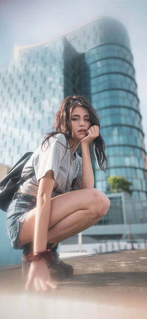 年輕女性在現代玻璃建築前若有所思地蹲著。 — 曼谷 壁紙