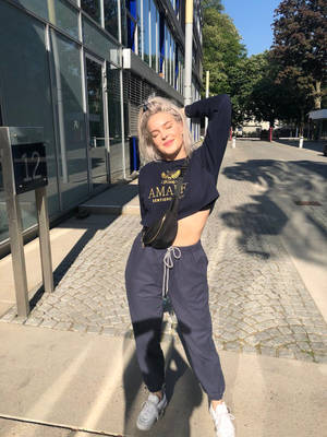 年輕女性穿著休閒街頭服飾，在現代建築附近的陽光人行道上擺姿勢。 — 安妮與艾比 壁紙
