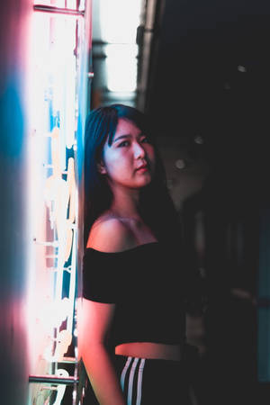 年輕女性站在黑暗城市小巷中發光的霓虹燈牌旁。 — 霓虹燈 壁紙
