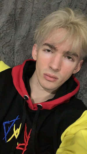 年輕金髮男子穿著彩色連帽衫，背景為灰色牆壁。 — 火之翼 壁紙