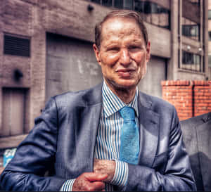 一位穿著西裝和藍色領帶的年長男士在城市環境中自信地微笑。 — 羅素·衛斯特布魯克 壁紙