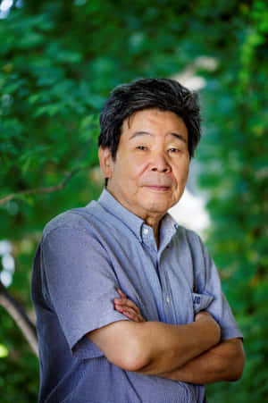 一位穿著藍色格紋襯衫的年長男性在綠色戶外環境中交叉雙臂站立。 — 花子君 壁紙
