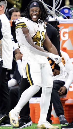 身穿白色和金色球衣的足球員在球場上慶祝。 — Alvin Kamara 壁紙