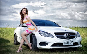 穿著條紋連衣裙的女子在草地上白色賓士汽車旁擺姿勢，背景有風力發電機。 — 模特兒 壁紙